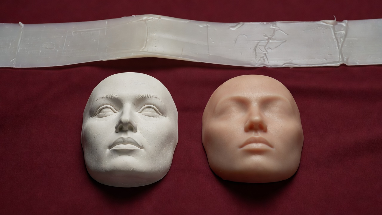 Soft-lit 3D render of a plaster face mould and a silicone prosthetic piece on a burgundy background